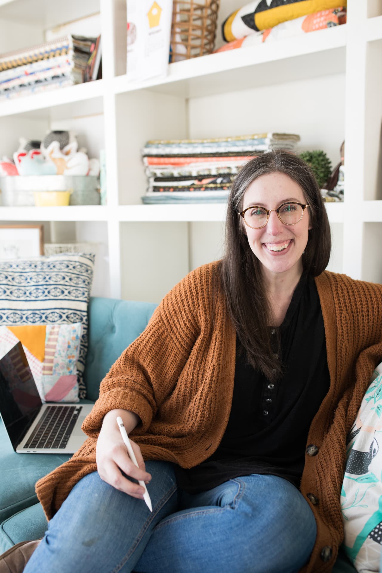 Stacie Bloomfield sitting on a couch with her laptop and stylus in a bright studio