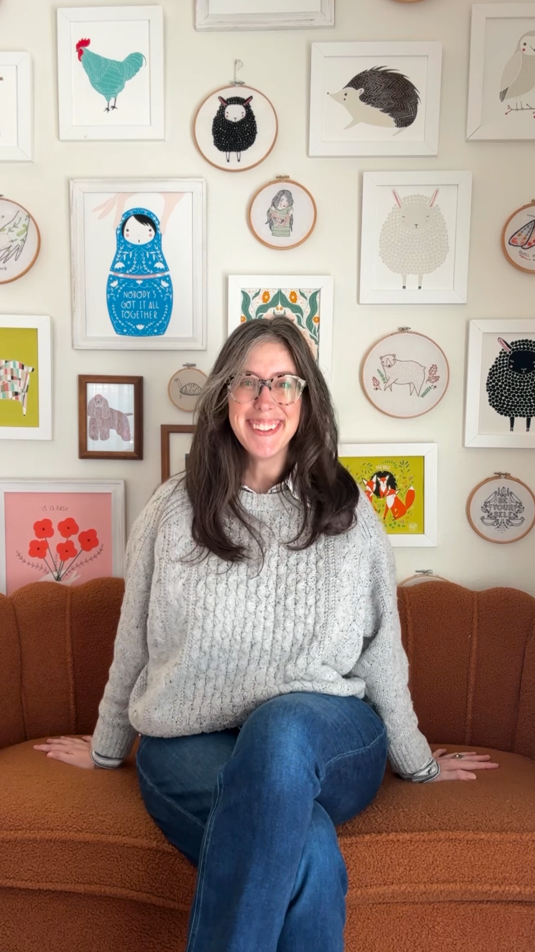 Stacie Bloomfield sitting on a terracotta couch in front of a gallery wall of her art